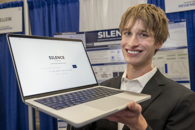 Official ISEF photo of Evan holding an open laptop displaying the SILENCE software interface, with the SILENCE poster and Regeneron/CELL036 booth signage behind him