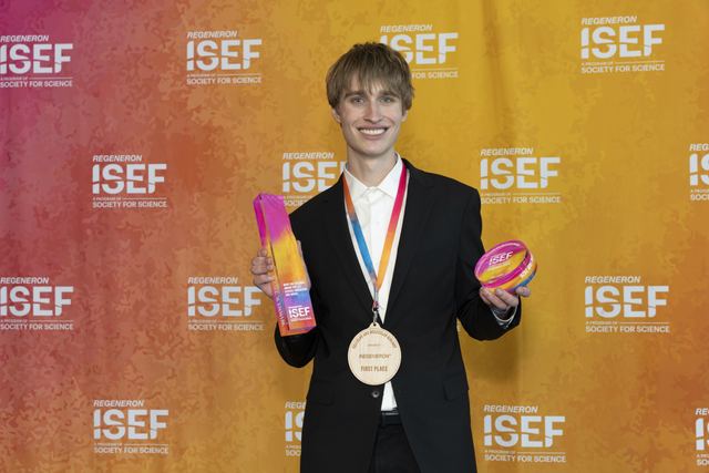 Official backstage awards portrait of Evan against the Regeneron ISEF step-and-repeat backdrop, wearing the first-place gold medal and holding his trophy and award disc