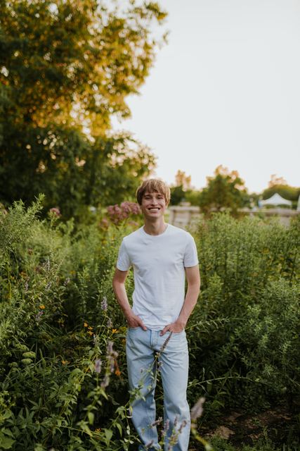 Smiling full-body portrait of Evan among tall wildflowers and prairie plants at golden hour, natural, cheerful, subtly echoes his plant/greenhouse interest