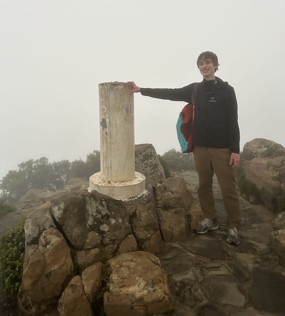 Evan Morris beside the summit marker on a fog-covered mountaintop