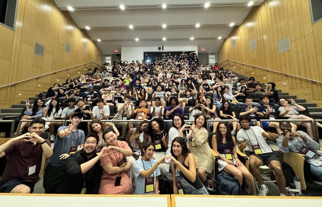 Evan's Yale Young Global Scholars cohort filling a lecture hall, making heart and peace signs for a group photo