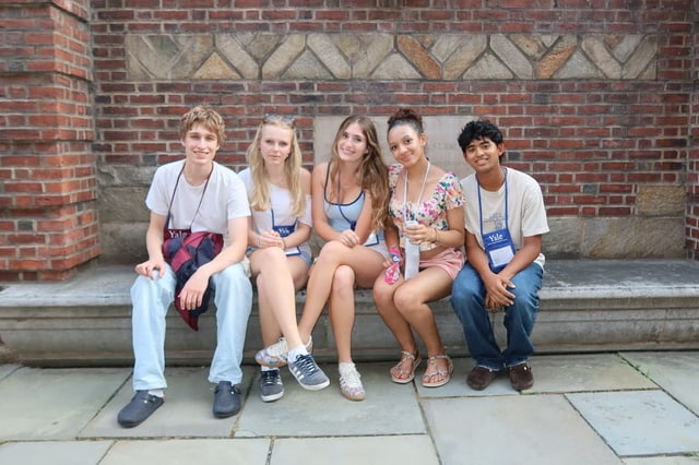 Evan Morris with four friends on a stone bench against a brick wall at Yale