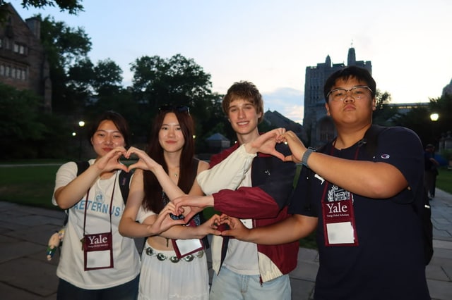 Evan Morris and three friends making heart shapes with their hands on the Yale campus at dusk