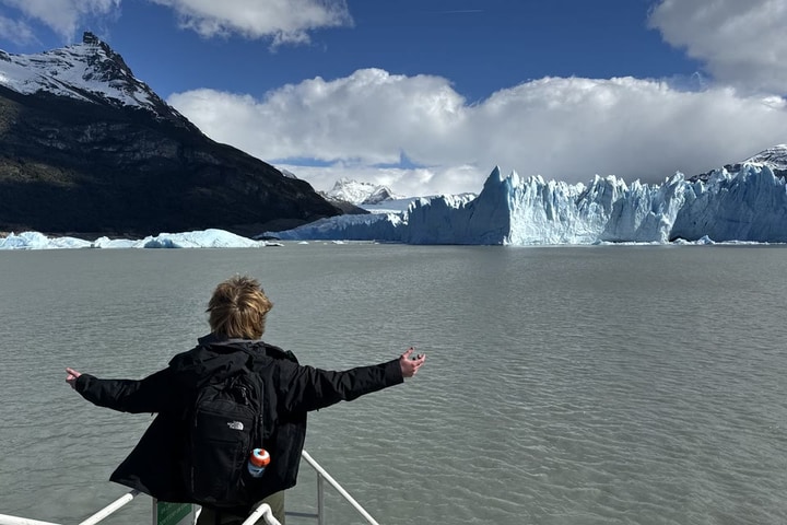 Evan Morris at the rail of a boat with his arms spread wide, facing the Perito Moreno Glacier in Patagonia