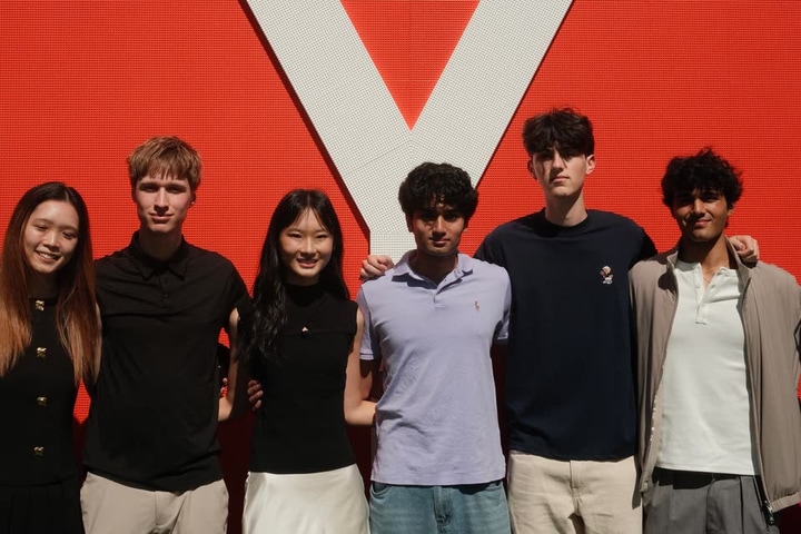 Evan Morris, second from left, with five other students in front of the Y Combinator logo on a red wall